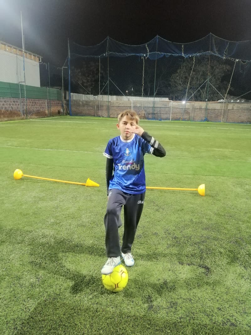 Alumno con el pie sobre el balón entre conos, en un entrenamiento de noche